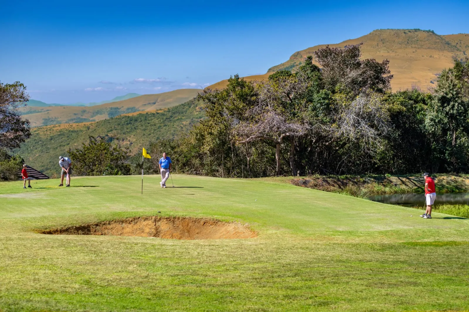 Players on a green with the escarpment behind